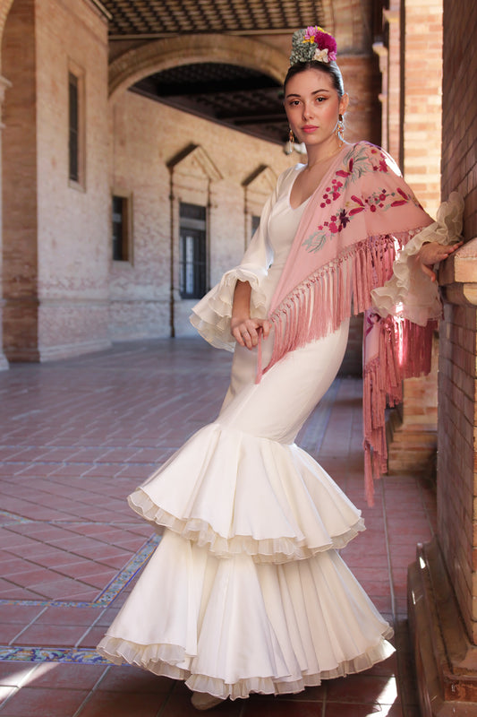 Brilla en la Feria de Abril con el vestido de flamenca marfil Jazmín, acompañado de un mantón rosa con flor buganvilla, ramillete de flores Duende y pendientes dorados Jara. Un look lleno de elegancia y fuerza flamenca.