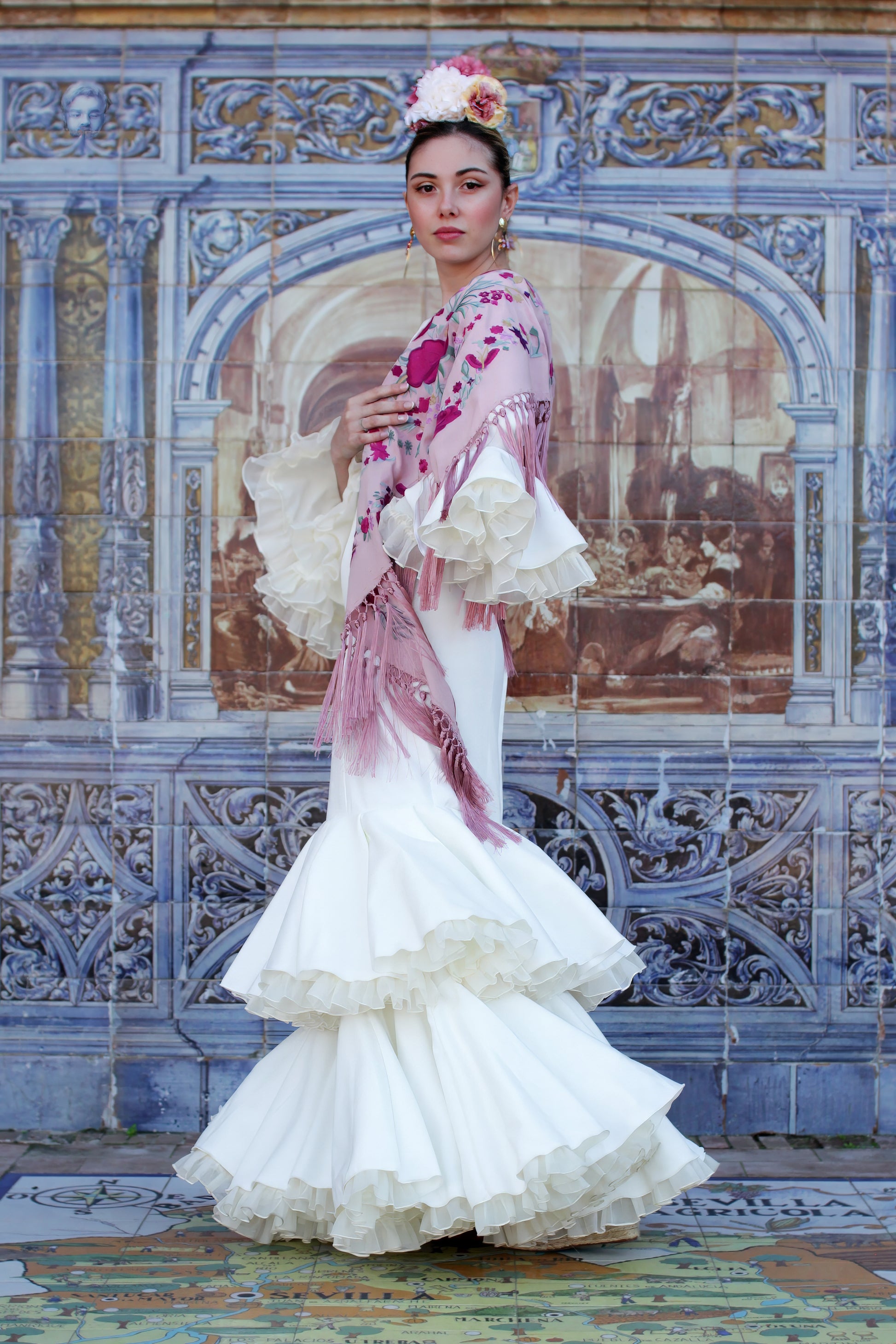 El vestido de flamenca marfil Jazmin es la eleccion perfecta para la Feria de Abril. Con un manton rosa con flor buganvilla, ramillete Duende y pendientes dorados Jara, este look flamenco destaca por su elegancia y estilo unico.