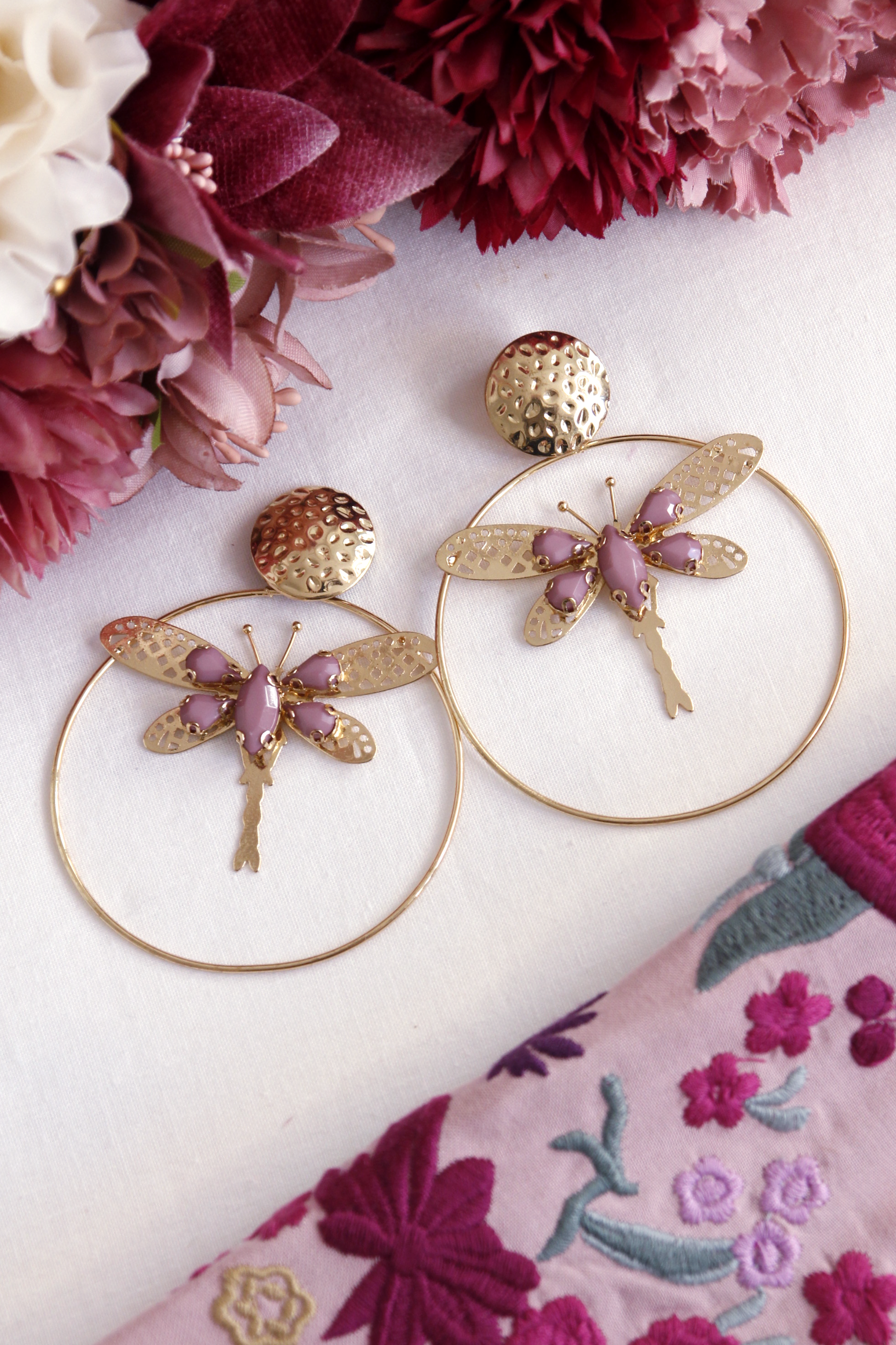 Los pendientes Jara combinan la elegancia del aro dorado con una libélula dorada decorada con detalles malva. Un accesorio único y sofisticado para añadir frescura y delicadeza a tu look flamenco.